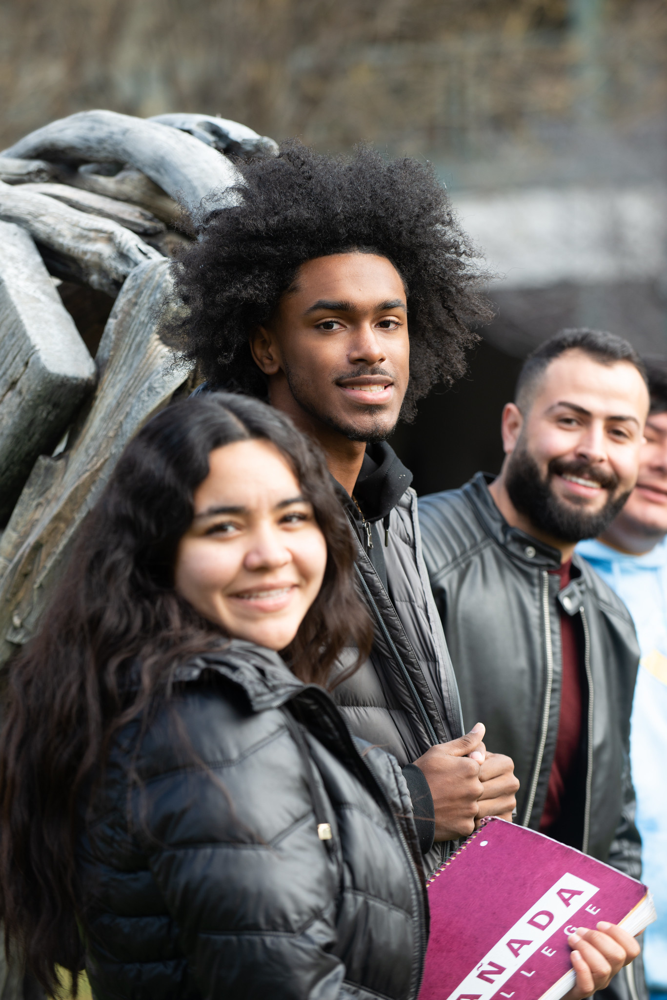 Students smiling at the viewer and holding a Cañada College folder.